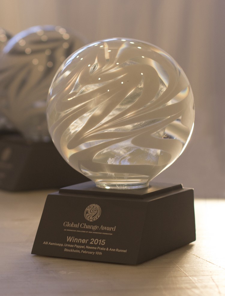 Närbild av statyetten, glasklot med vit slingrande färg på en mörkgrå sockel med vinklad framkant. Logotyp med Global Change Award